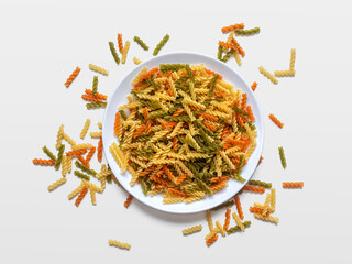 Multicolored spiral fusilli pasta in and around a white plate