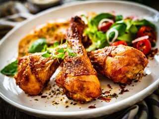 Barbecue chicken drumsticks with fried potato, lettuce and mini tomatoes on wooden table

