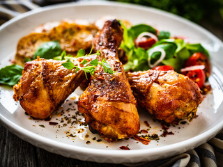 Barbecue chicken drumsticks with fried potato, lettuce and mini tomatoes on wooden table
