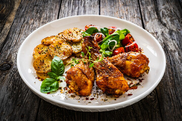 Barbecue chicken drumsticks with fried potato, lettuce and mini tomatoes on wooden table
