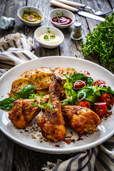 Barbecue chicken drumsticks with fried potato, lettuce and mini tomatoes on wooden table
