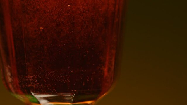 Close up of an alcoholic drink in transparent glass. Stock clip. Alcohol beverage isolated on a colorful wall background.