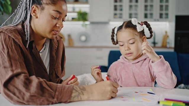 Young happy african american mother drawing picture with little daughter, spending time together at home, tracking shot