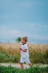The boy runs against the background of a wheat field and blue sky. Ukrainian land. Child in nature. Relaxation.
