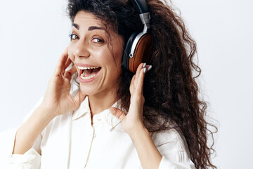 Headshot of smiling Curly Beautiful Latin Woman Listening Cool Playlist In Headphones Singing Look At Camera Isolated At White Studio Wall Background. Music Devices DJ Technologies Huge Sale Concept