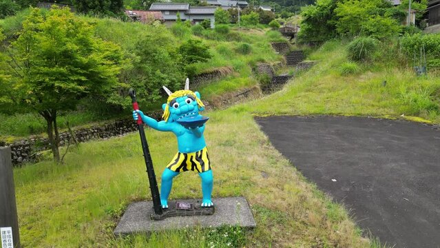 Rise and tilt down on blue oni demon character and Japanese mountain town