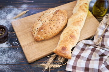 Fresh bread loaf and baguette on wooden cutting board at kitchen table