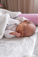 Fototapeta na wymiar cute little newborn baby girl peacefully sleeps in the nursery on a white cotton bed. vertical