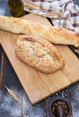 Fresh bread loaf and baguette on wooden cutting board at kitchen table