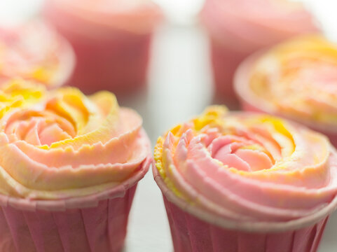 Closeup of delicious cupcakes with pink yellow buttercream frosting decorated as rose flowers. Sweet candy bar background