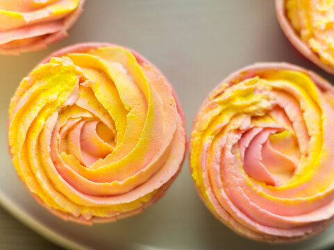 Closeup from above view of delicious handmade cupcakes with pink yellow cream made as rose flowers. Sweet candy bar background