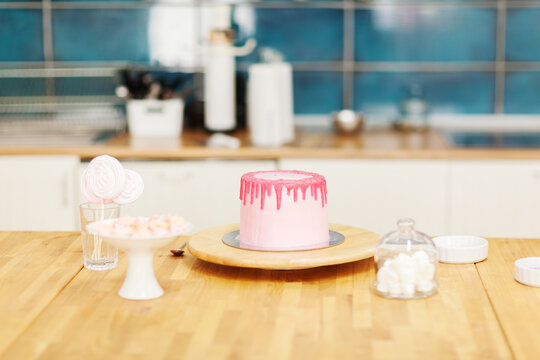 Unfinished drip cake on rotating stand, meringues and marshmallows on table in bakery shop or pastry cafe kitchen
