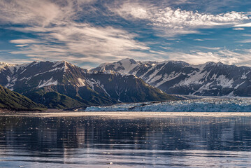 Disenchantment Bay, Alaska, USA - July 21, 2011: Under blue cloudscape, landing of Hubbard glacier forms blue ice wall on dark water with range of snow covered mountains behind it.