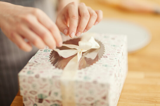 Hands of unrecognizable female  bakery chef or saleswoman packing cupcakes into gift box and tying it with ribbon, closeup