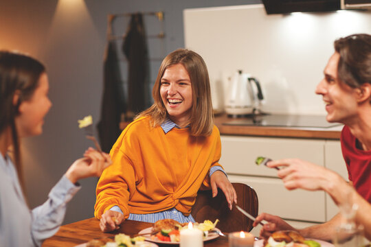Happy young woman laughing joyfully while having cheerful talk with friends over dinner at home, selective focus