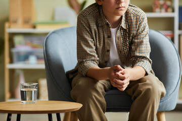 Close-up of teenage boy sitting on armchair at psychotherapist office and having individual session