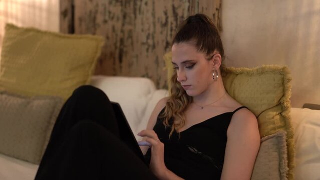 Chica delgada con pelo largo en habitación de hotel con encanto sobre la cama con tablet y smarpthone