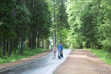 Fototapeta premium A family, a man and a woman with a child in a baby carriage walk in the park in summer.