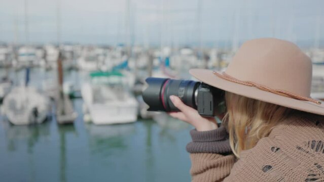 Female photographer takes pictures of yachts and boats in the docks. Beautiful woman in stylish outfit enjoying summer vacation at the ocean shore. High quality 4k footage