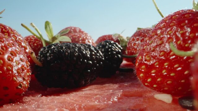 Strawberries in a row lie on a cut watermelon, against a blue sky. Mulberry falls. Dolly slider extreme close-up. Laowa Probe. Slow mo