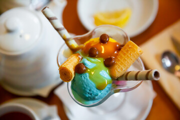 Balls of yellow and blue ice cream with waffle tube in glass ramekin on table. Top view