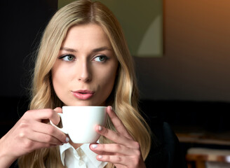 Portrait of a beautiful young blonde girl. White woman drinking coffee latte with confident eyes. Face close up view. Morning summer mood