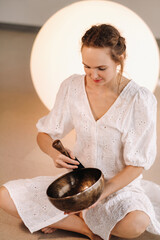Portrait of a female yoga teacher playing a Tibetan bowl or singing a bell in the gym during a yoga...
