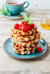 Stack of belgian waffles with honey, mint and fresh raspberries on turqouise plate