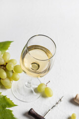A glass of white wine on white textured background with corkscrew, grapes and corks. Text space