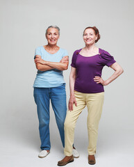 Two pretty older women friends on grey background.