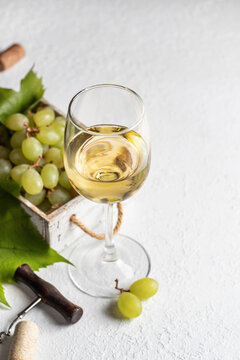 White wine glass still life with grapes in wooden box, corkscrew on white textured background. Text space right
