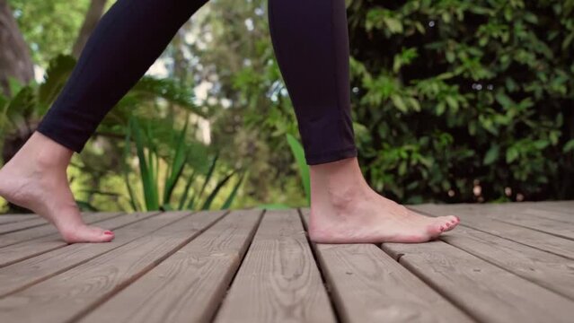 Slow motion of young woman walking barefoot on wooden deck in nature. Blurred background camera traveling.