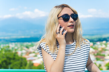 blond Caucasian girl with sunglasses talking on a phone, medium closeup outdoor. High quality photo