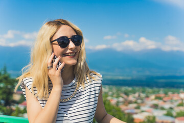 blond European girl talking on a phone and laughing in the park, medium closeup. High quality photo