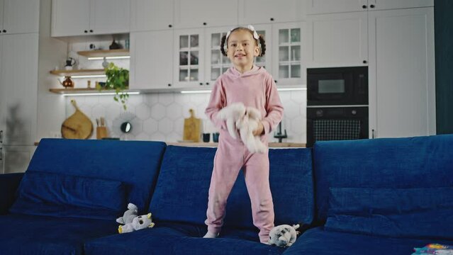 Adorable little african american girl humping on couch at home, fooling around on sofa, slow motion