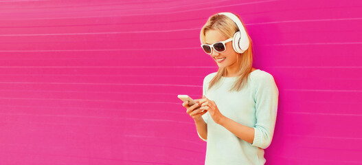 Portrait of happy smiling young woman in headphones listening to music with smartphone on pink background, blank copy space for advertising text