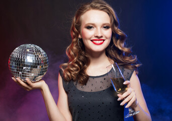 Fototapeta premium Beautiful woman in evening dresses, chic hairstyles and makeup holding a disco ball and glasses with champagne.