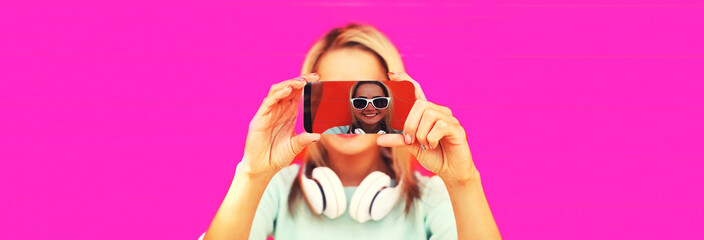 Close up of woman stretching her hands taking selfie with smartphone in headphones listening to music on pink background