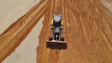 Horizontal aerial outdoor shot. Bulldozer during works at a road construction site leaving track marks in the sand. . High quality photo © PoppyPix