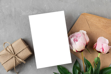 Greeting or invitation card with pink peony flowers, gift box and envelope on gray background. Mock...