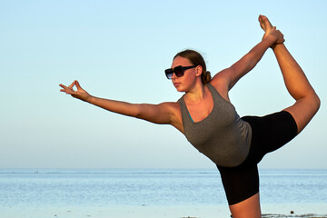 Young healthy woman practicing and workout yoga on the beach at sunset, benefits of natural environments for physical activity.