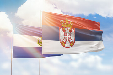 Sunny blue sky and flags of serbia and el salvador