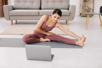 Sporty young woman practicing yoga in front of laptop, watching online tutorials. © anatoliycherkas
