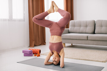 Attractive young woman stands on her head and upside down and doing fitness exercises at home.