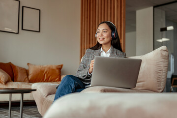 Asian business woman listening music sitting with laptop during break in cozy office