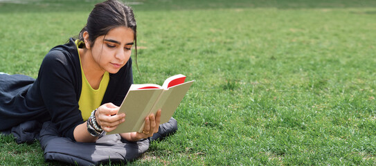 Young girl lying on green grass reading book web banner