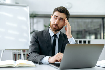 Pensive Caucasian male with a beard, director of company, top manager, sits at a desk in front of a...