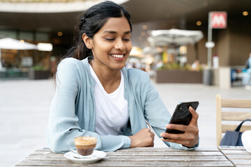Smiling Indian woman holding cell phone communication online, reading text message sitting in cafe....