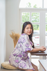 Portrait piceture of an Asian woman in a white patterned dress sitting and looking at a camera in a cafe