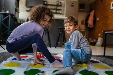 Brother and sister siblings small caucasian boy and girl child play twister game on the floor at...